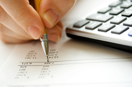 A hand holding a pen pointing to sums with a calculator in the background