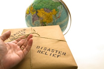 Hand holding brown paper parcel, with the words disaster relief written on it in front of a globe.
